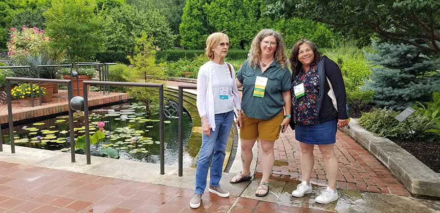Group of three standing women in the garden next to the lily water feature