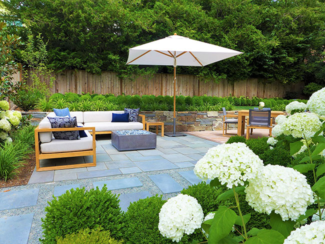 Patio with umbrella and outdoor sofas, firepit and table and chairs on slate and gravel with surrounding plantings.