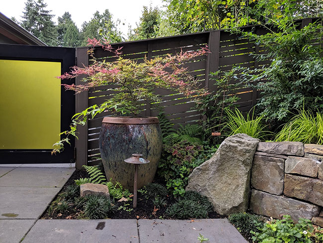 Side yard of same home with rock wall, large concrete pavers, large container with plant, fence and gate