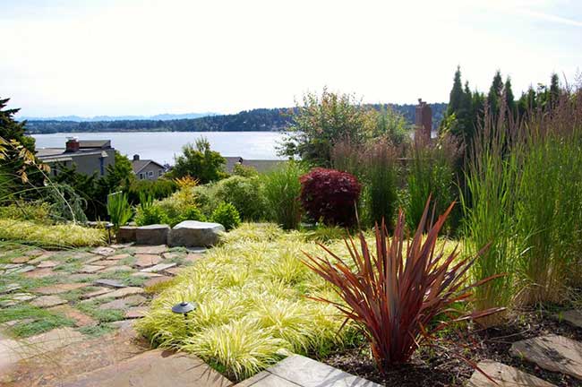 A stone patio surrounded by colorful plantings overlooks Lake Washington.