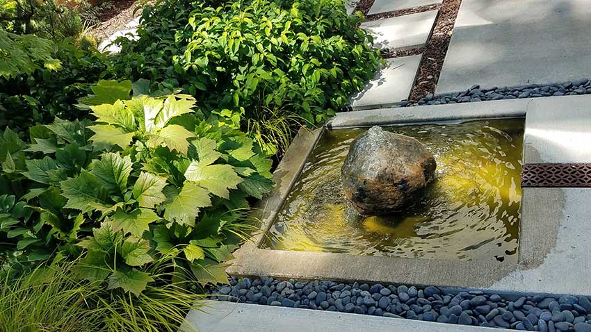 A water feature set into a paving stone patio includes a long channel.