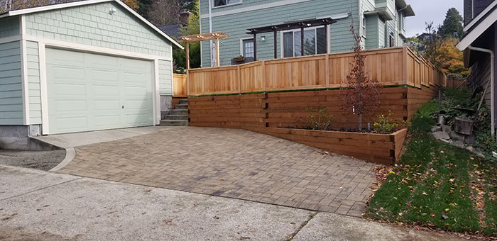 The same image shows the boxwoods replaced with a permeable paver driveway and retaining walls made of pressure treated lumber topped with a short fence.