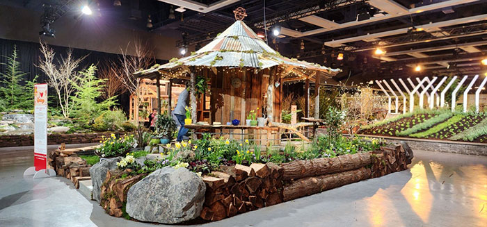 Devonshire Landscape’s entry for the 2024 Flower and Garden Festival features natural log retaining walls, a semi-open garden shed and beds planted with flowering bulbs and perennials.