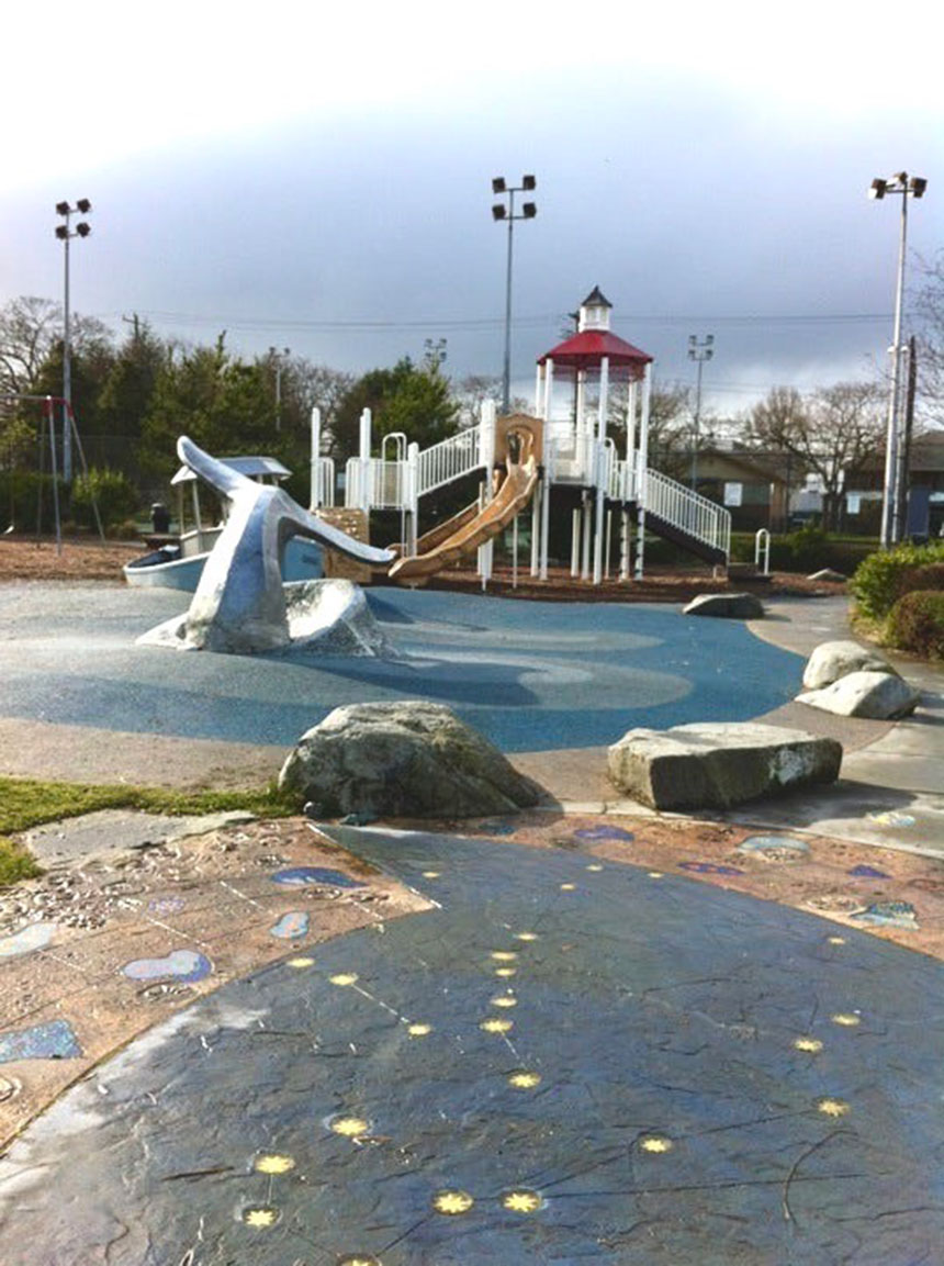 A children’s playground features a play structure, a climbable sculpture of a whale tail and ‘swimming stars’ set into the concrete path.